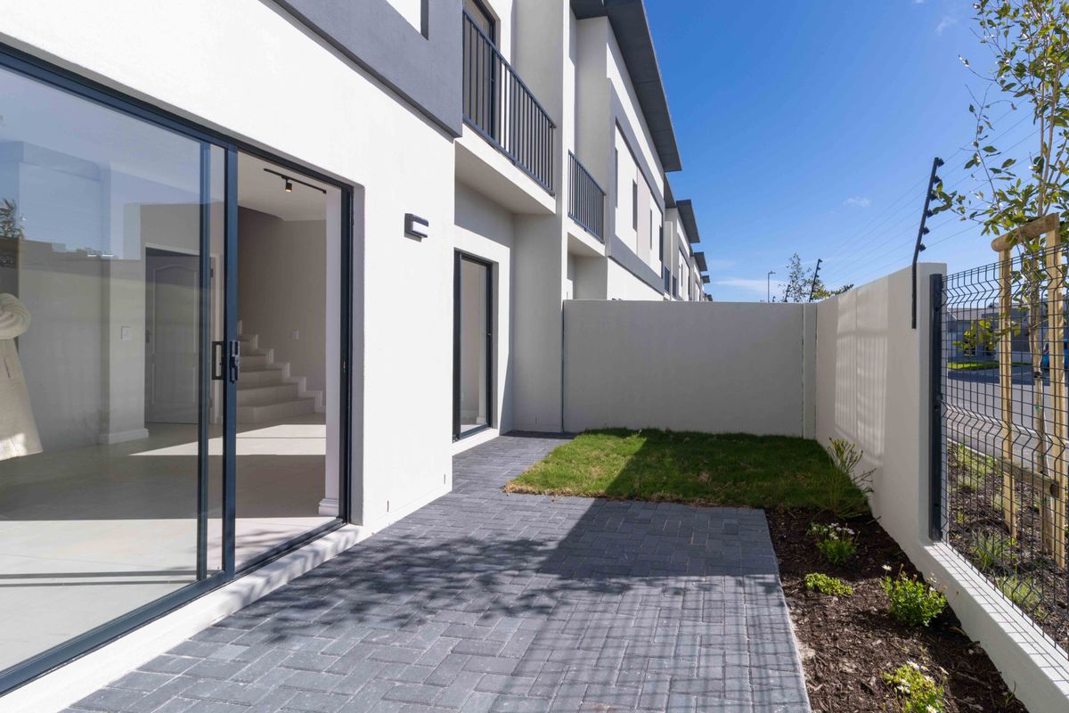 Modern townhouse rear exterior featuring a paved patio, small garden area, boundary wall with electric fencing, and sliding glass doors leading to the interior.