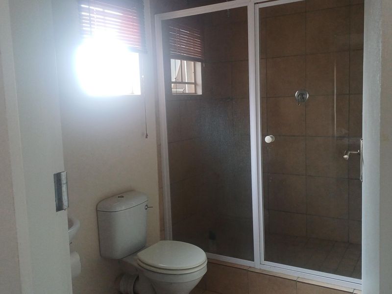 A functional bathroom featuring a shower enclosure, toilet, and tiled finishes, illuminated by natural light from the window.