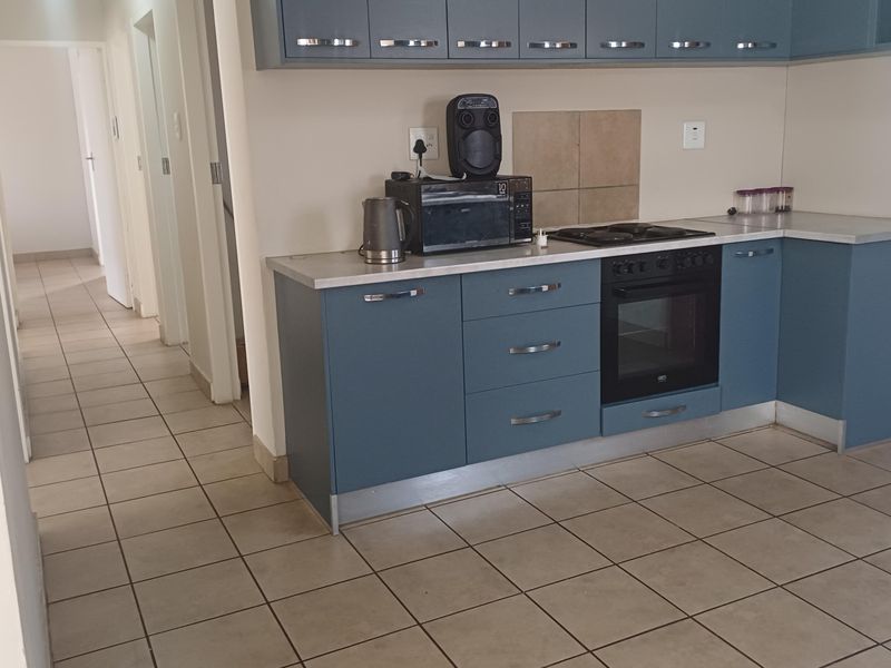A functional kitchen featuring blue cabinetry, laminate countertops, built-in oven and hob, and tiled flooring, with an adjacent hallway leading to other rooms.