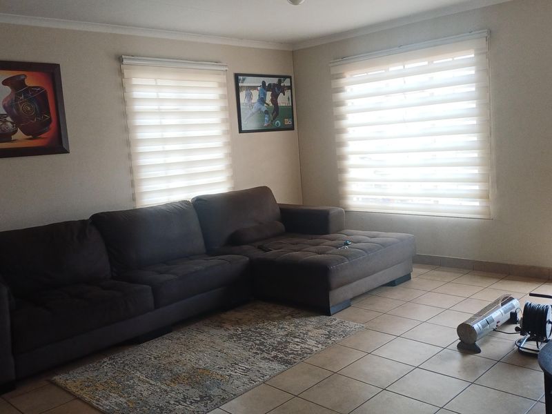 A comfortable living room featuring tiled flooring, neutral wall tones, and dual roller blinds providing natural light control.