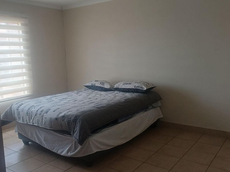 A simple bedroom featuring neutral walls, tiled flooring, and a window fitted with a roller blind.