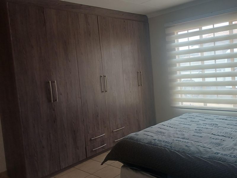 A bedroom featuring dark wood-finish built-in cupboards, tiled flooring, and modern roller blinds, providing ample storage and natural light.