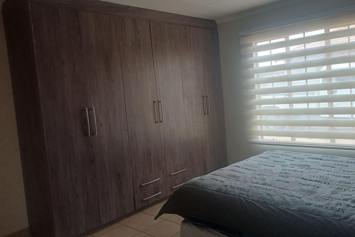 A bedroom featuring dark wood-finish built-in cupboards, tiled flooring, and modern roller blinds, providing ample storage and natural light.