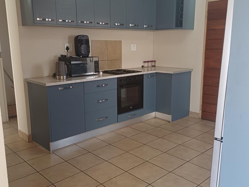A functional kitchen featuring blue built-in cabinetry, laminate countertops, a built-in oven with electric hob, and tiled flooring.