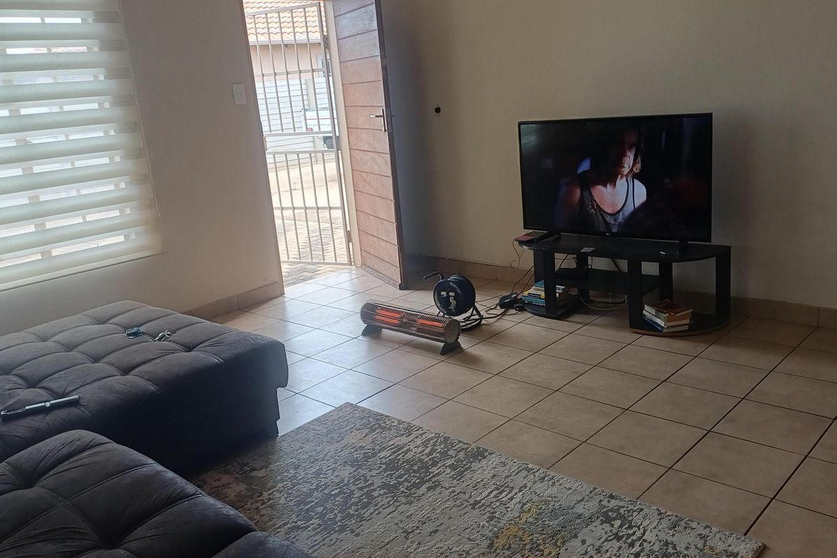 A living room featuring tiled flooring and roller blinds, with direct access to the exterior through a security gate.