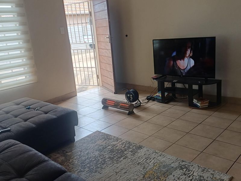 A living room featuring tiled flooring and roller blinds, with direct access to the exterior through a security gate.