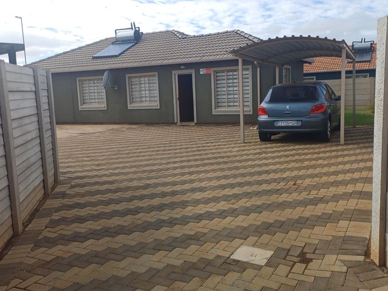 Front exterior view of the house featuring a paved driveway, a covered carport, and a solar water heating system installed on the tiled roof.
