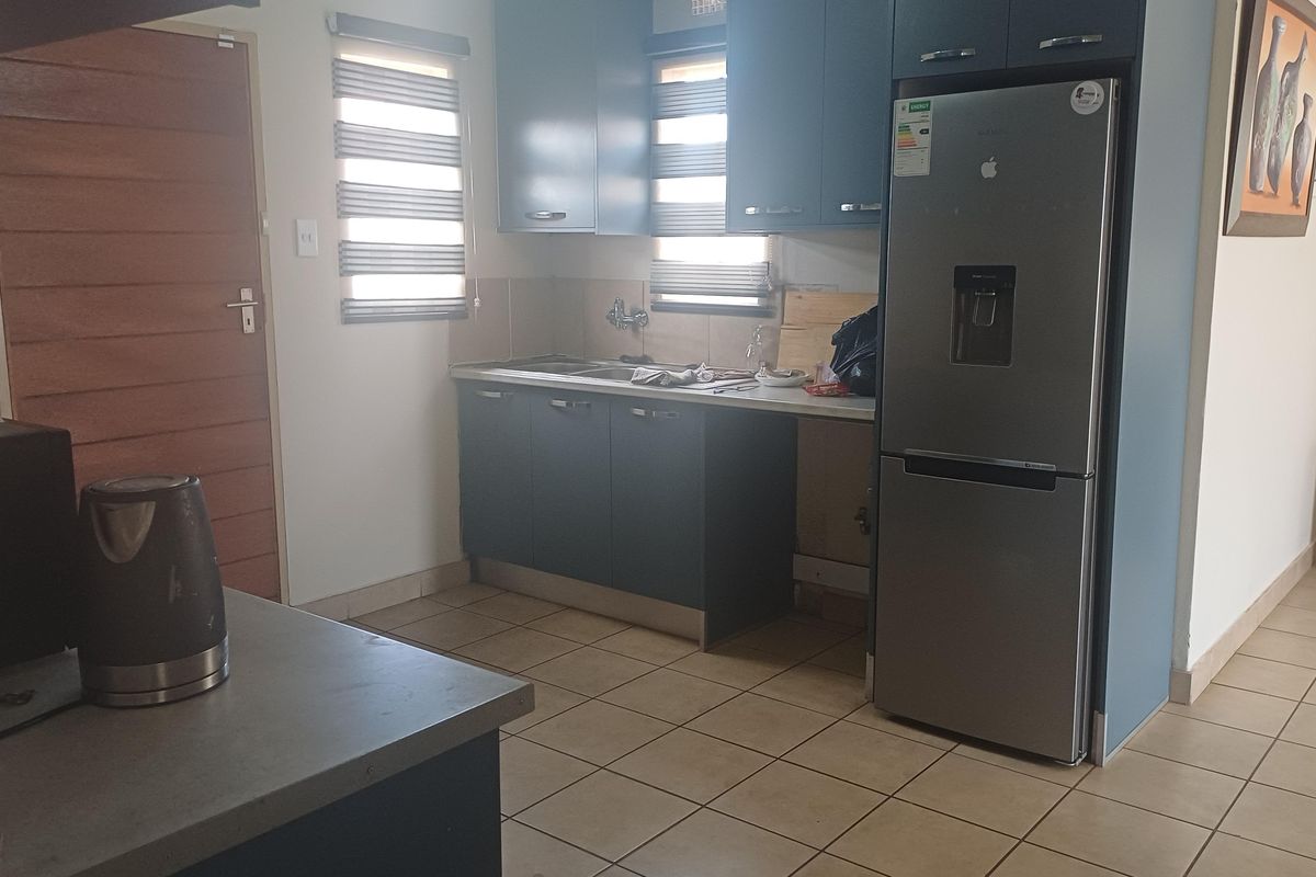 A functional kitchen featuring dark blue cabinetry, tiled flooring, and a stainless steel sink, with space for a full-sized refrigerator.