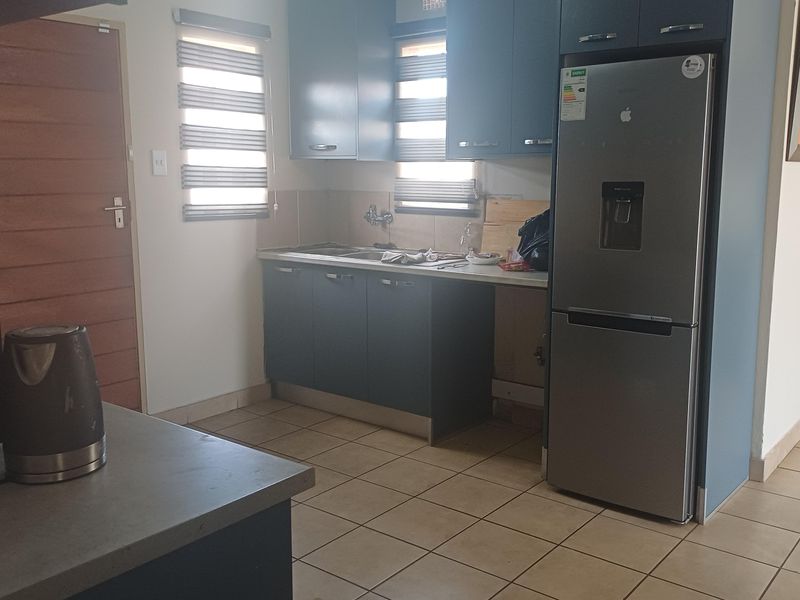 A functional kitchen featuring dark blue cabinetry, tiled flooring, and a stainless steel sink, with space for a full-sized refrigerator.