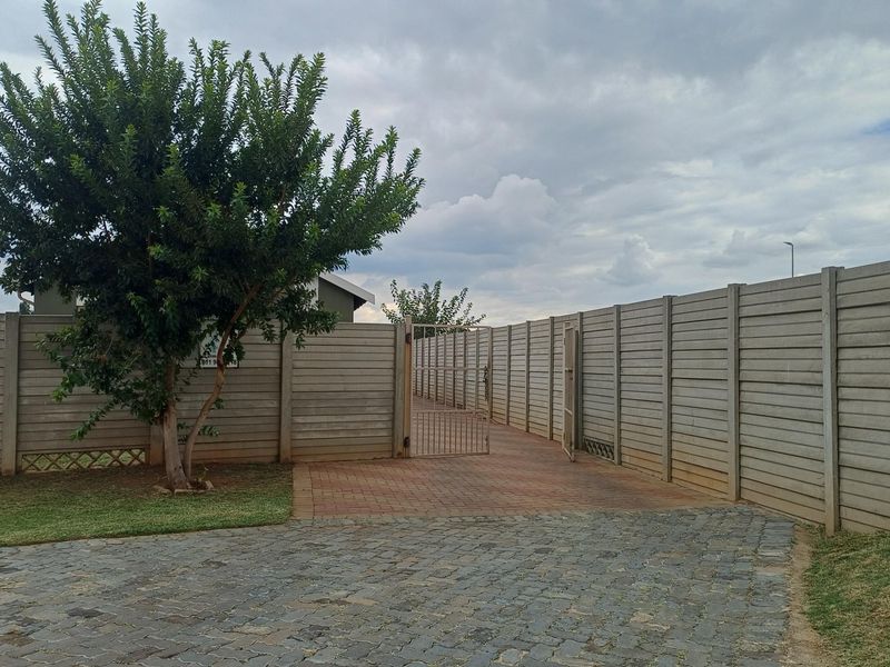 A private rear outdoor area featuring a paved driveway, cobblestone accents, and secure precast concrete boundary walls with a metal pedestrian gate.