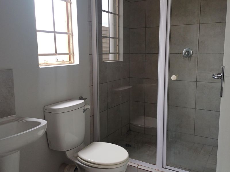 A functional bathroom featuring a pedestal basin, toilet, and a tiled shower enclosure with a glass door.