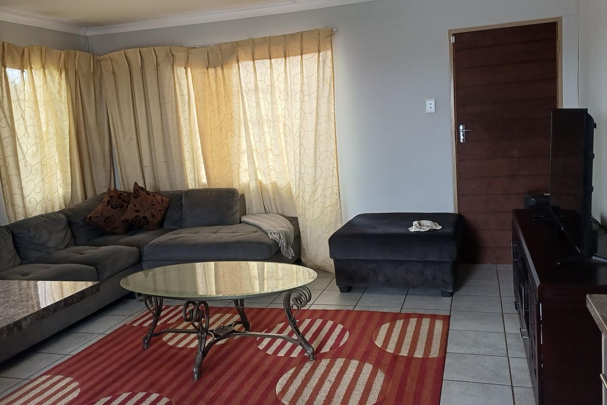 A living room featuring tiled flooring, cove cornicing, and a timber door, providing a functional and neutral space for relaxation.