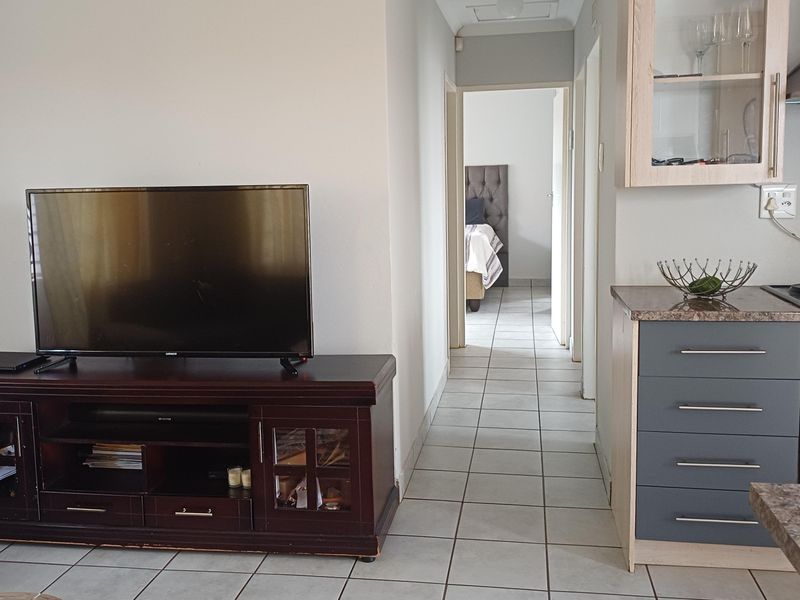 Open plan living area featuring tiled flooring, connecting to a kitchen with built-in cabinetry, oven, and extractor fan, leading to a hallway.