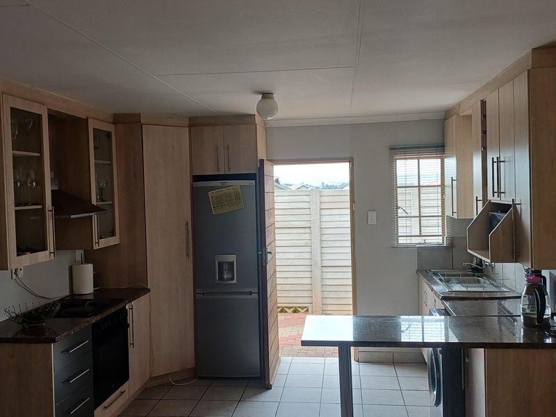 A functional kitchen featuring light wood-tone cabinetry, dark laminate countertops, tiled flooring, and direct access to an outdoor area.