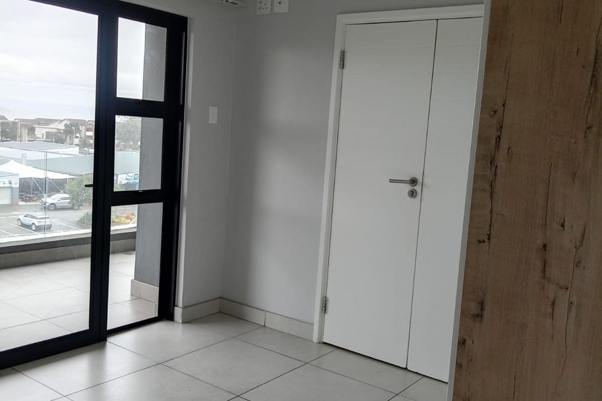 A bright, empty living area featuring neutral tiled flooring, modern double doors, and a large sliding glass door providing access to an outdoor balcony.