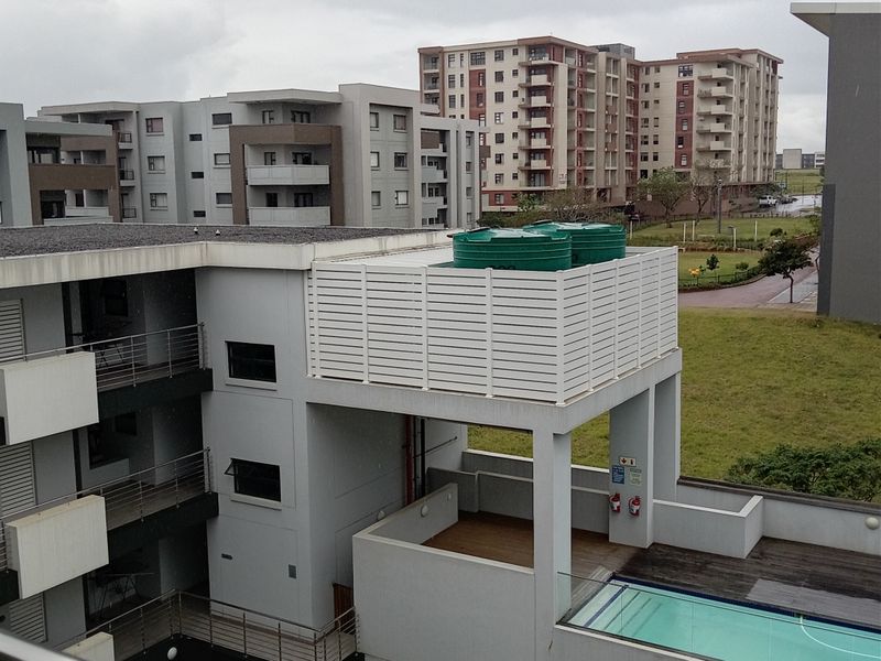 Aerial view of the apartment complex featuring a swimming pool, timber decking, and rooftop water storage tanks with privacy screening.