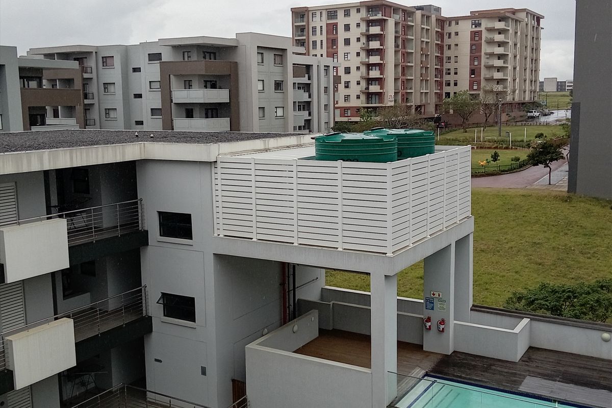 Aerial view of the apartment complex featuring a swimming pool, timber decking, and rooftop water storage tanks with privacy screening.