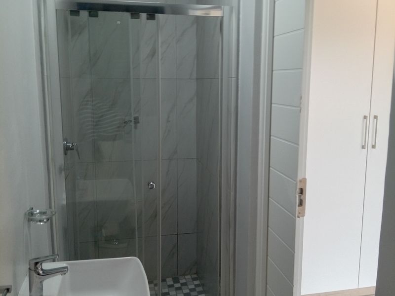 A modern bathroom featuring a glass-enclosed shower, a contemporary basin with a mixer tap, and neutral wall and floor tiling.