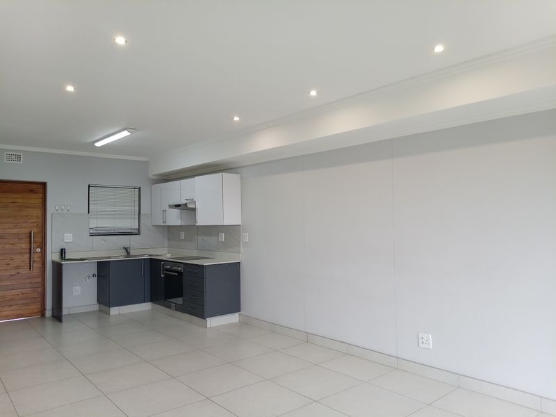 An open-plan living area featuring a modern kitchen with built-in cabinetry, integrated oven, extractor fan, and tiled flooring throughout.