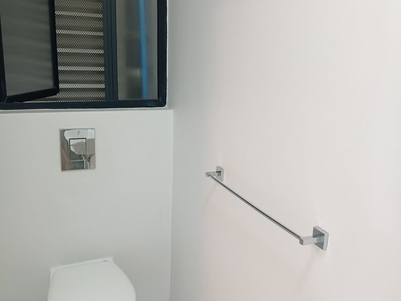 A clean and modern guest bathroom featuring a wall-mounted toilet, a compact basin with a mixer tap, and a chrome towel rail.