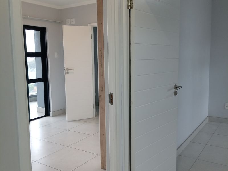 A bright, neutral hallway featuring tiled flooring and modern internal doors, providing access to adjacent rooms within the apartment.