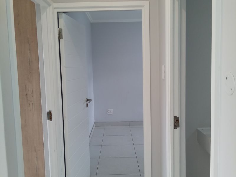 A clean, neutral hallway featuring tiled flooring and white internal doors leading to adjacent rooms within the apartment.