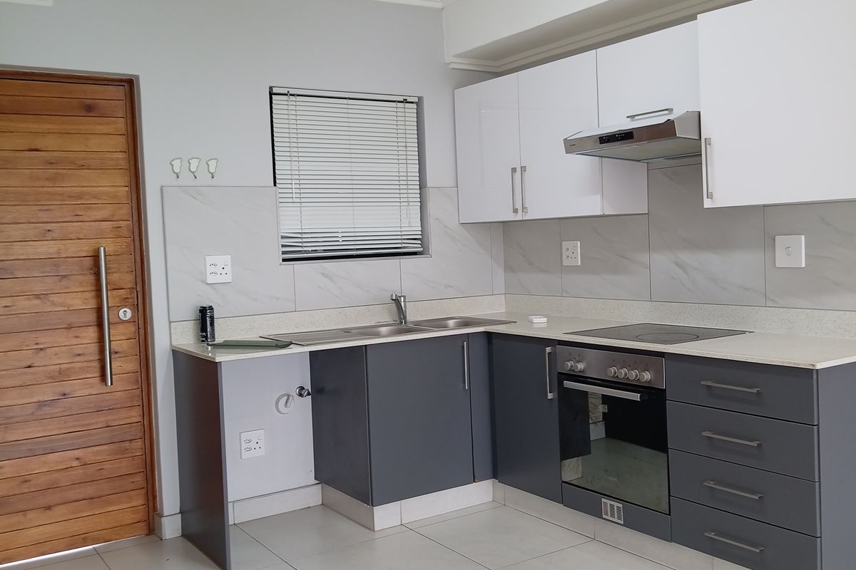 Modern kitchen featuring two-tone cabinetry, stone countertops, integrated oven and hob, and neutral tiled flooring in a clean, well-maintained space.