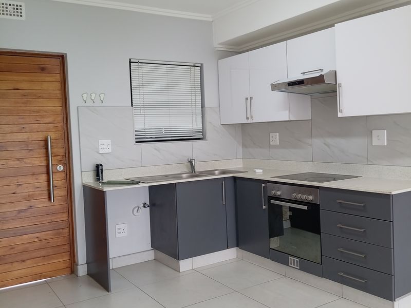 Modern kitchen featuring two-tone cabinetry, stone countertops, integrated oven and hob, and neutral tiled flooring in a clean, well-maintained space.