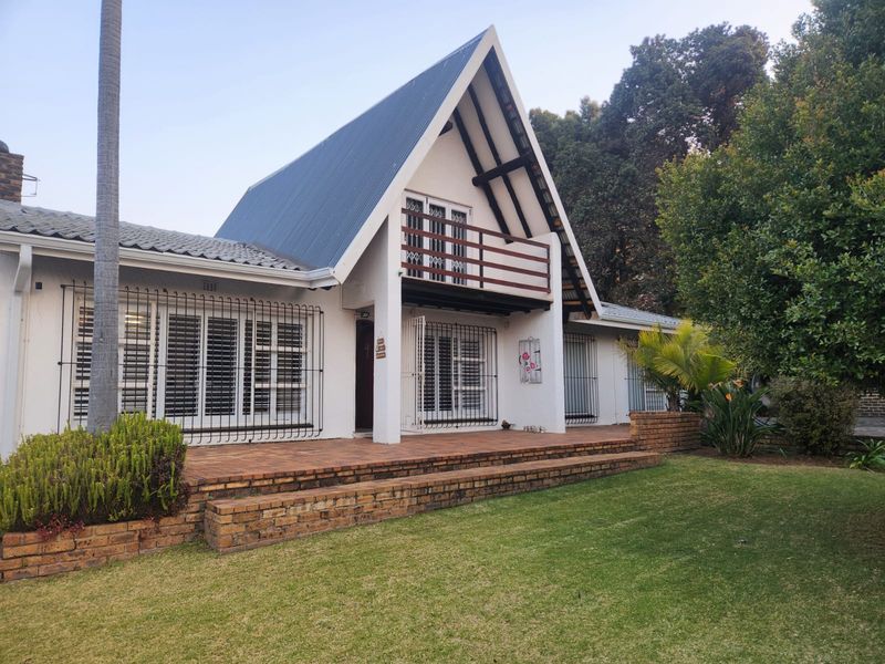 Rear view of an A-frame house featuring a brick patio, balcony, and established garden with security features on windows and doors.