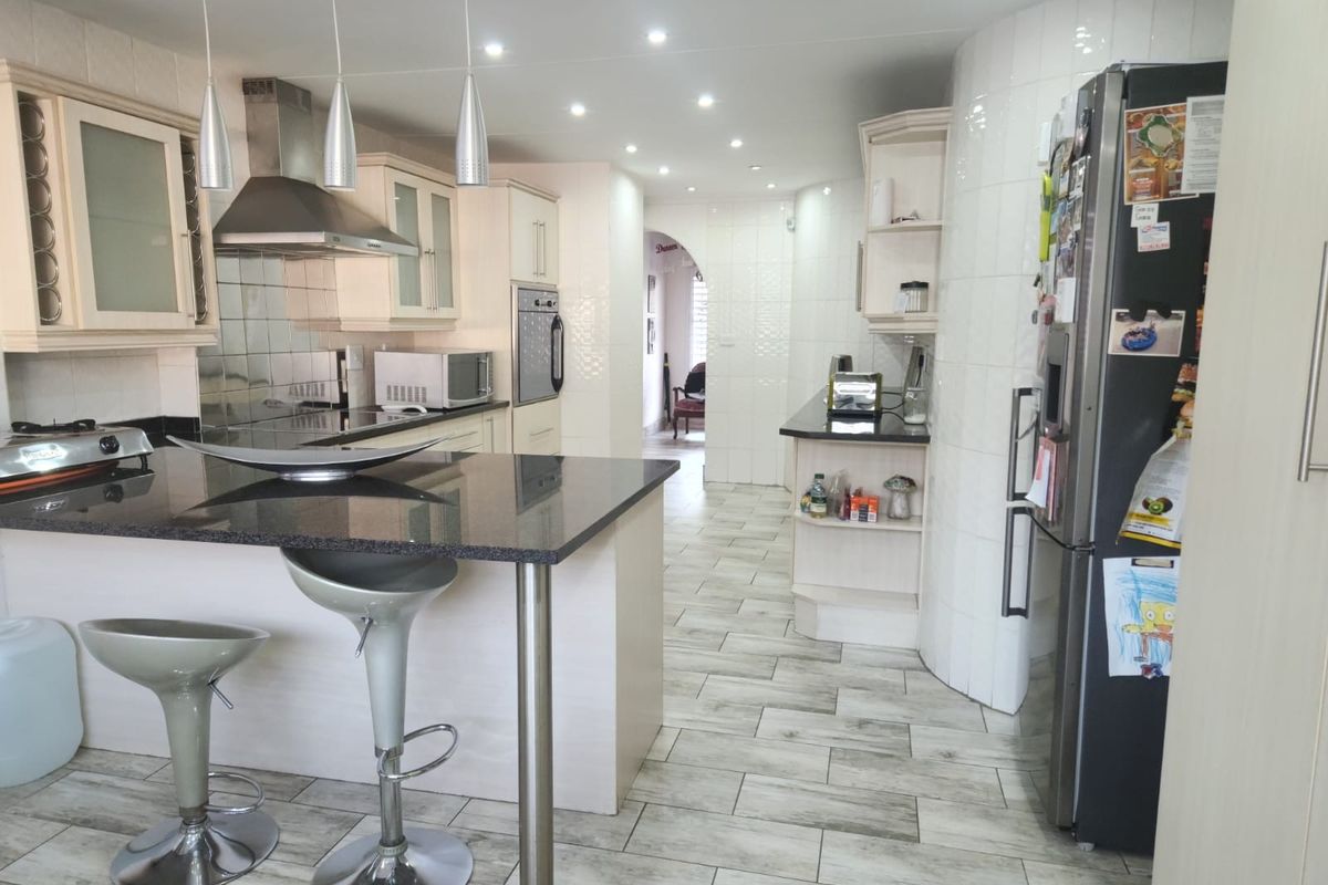 A well-lit kitchen featuring granite countertops, a central island with breakfast bar seating, built-in oven, and modern tiled flooring throughout.