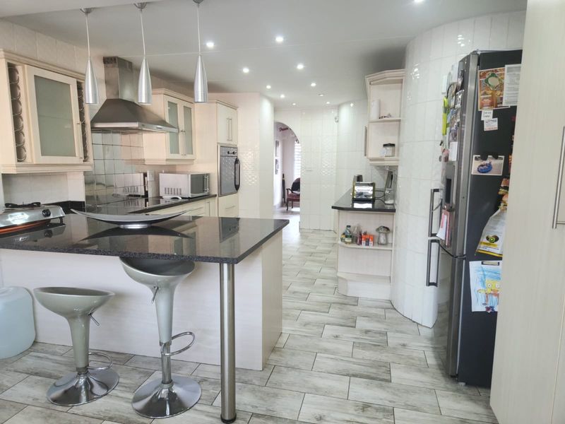 A well-lit kitchen featuring granite countertops, a central island with breakfast bar seating, built-in oven, and modern tiled flooring throughout.