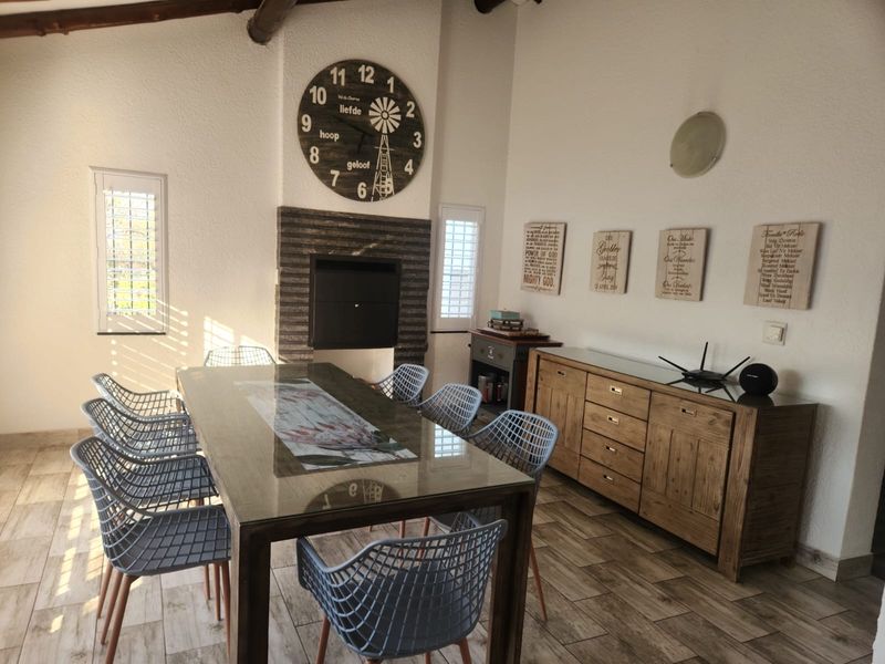 Dining room featuring a built-in fireplace with stone surround, exposed ceiling beam, tiled flooring, and plantation shutters.