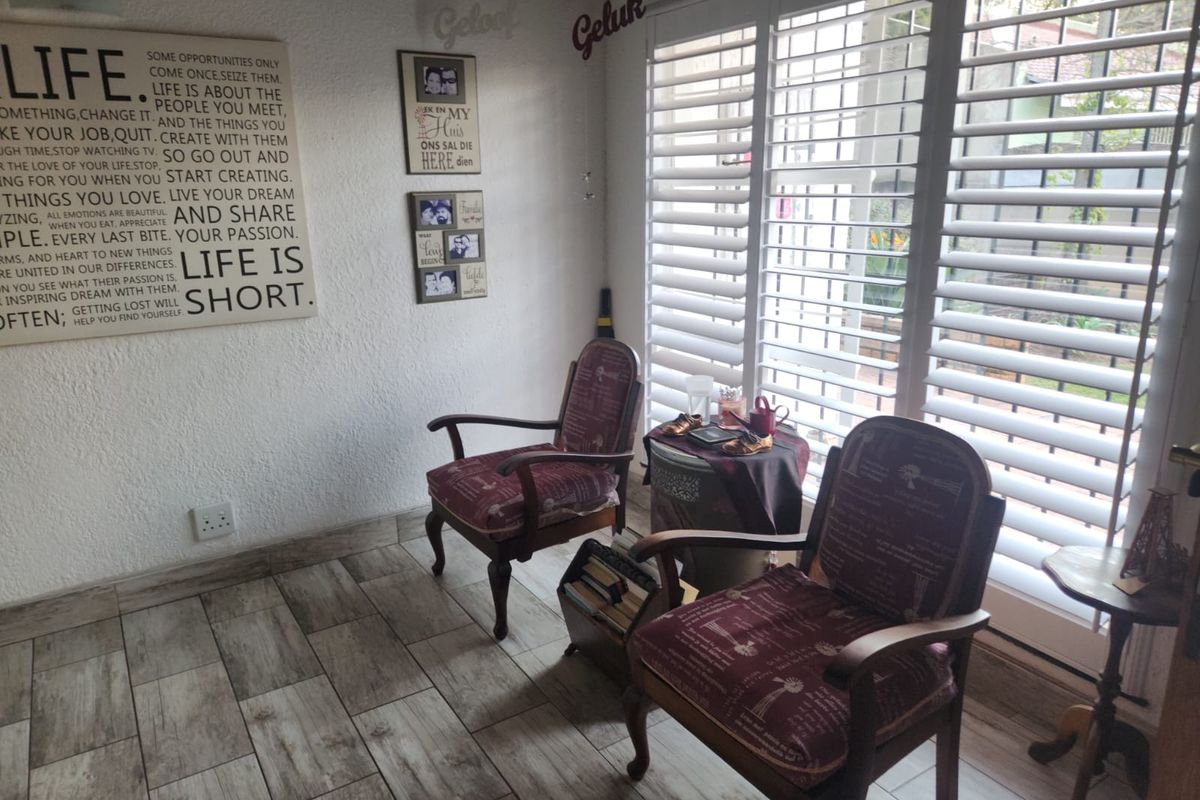 A cozy living area featuring wood-look tile flooring and white plantation shutters that provide natural light and privacy.