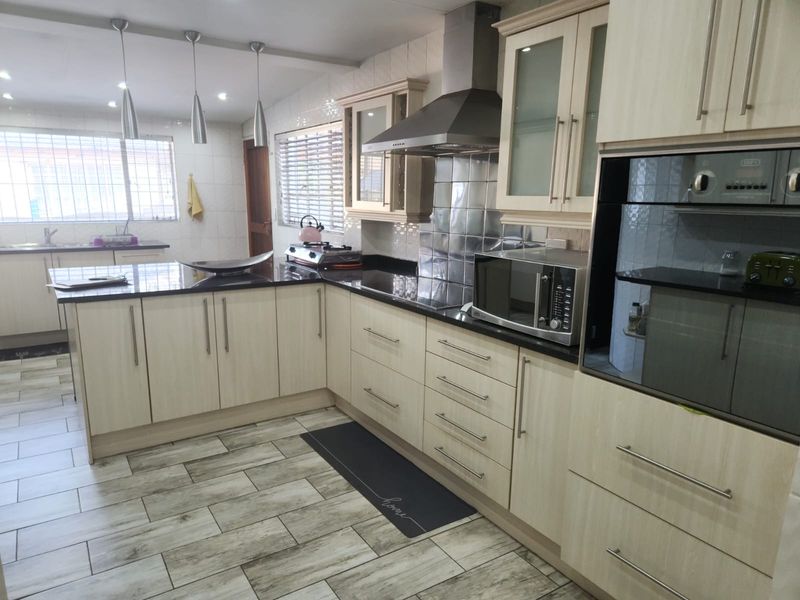 Modern kitchen featuring light wood-grain cabinetry, dark granite countertops, stainless steel appliances, and contemporary tiled flooring with ample workspace.