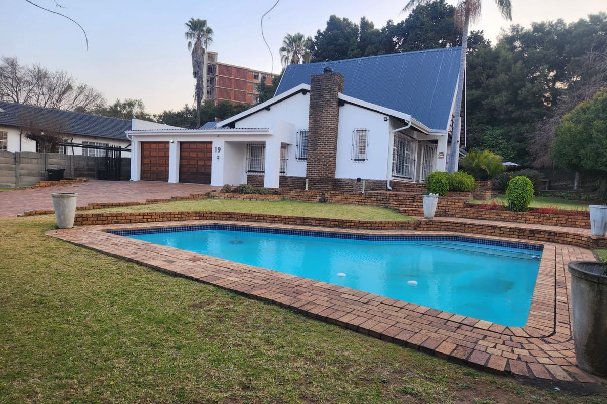 Rear view of the property featuring a swimming pool, brick-paved surround, landscaped garden, and a double garage with a pitched metal roof.