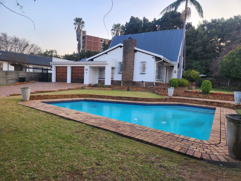 Rear view of the property featuring a swimming pool, brick-paved surround, landscaped garden, and a double garage with a pitched metal roof.