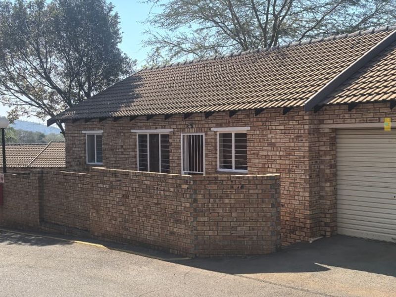 Front exterior view of a face brick townhouse featuring a tiled roof, secure window bars, and double roller shutter garage doors.