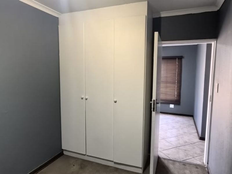 A compact bedroom featuring a built-in wardrobe, tiled flooring in the adjacent area, and venetian blinds, offering a functional space ready for personalization.