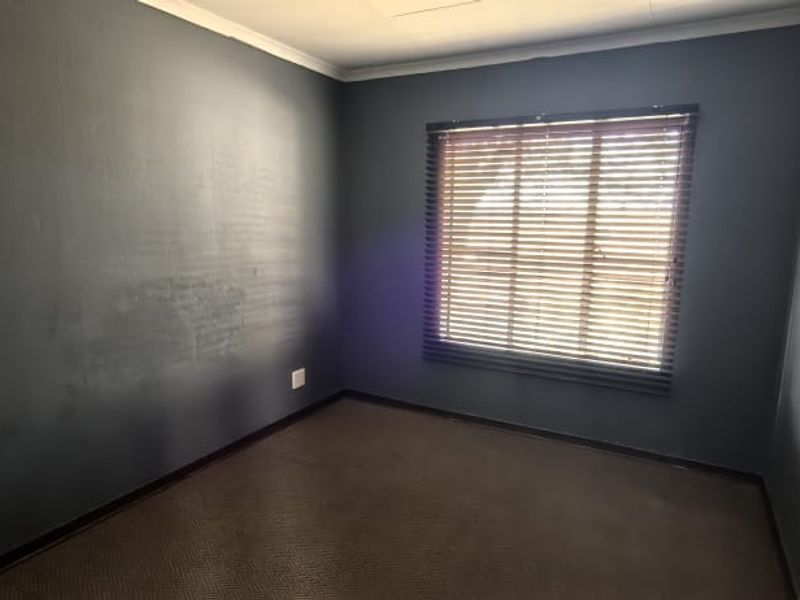 An empty bedroom featuring dark painted walls, carpeted flooring, and fitted venetian blinds, providing a blank canvas for potential interior design updates.