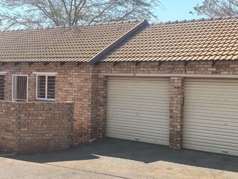 Front exterior view of a facebrick townhouse featuring a double garage with roller shutter doors and a tiled roof.