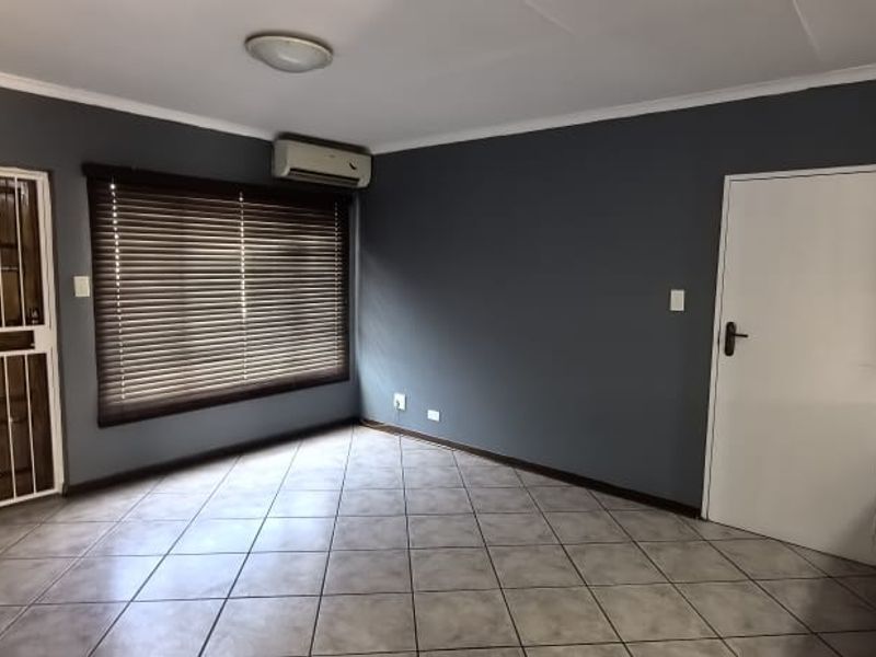 An empty living room featuring tiled flooring, an air conditioning unit, and a secure entrance door with a security gate.