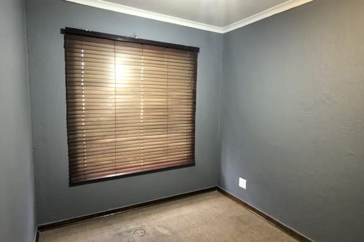 An empty bedroom featuring dark grey walls, carpeted flooring, and fitted venetian blinds.
