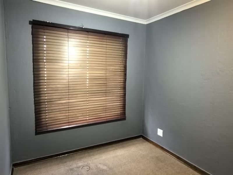 An empty bedroom featuring dark grey walls, carpeted flooring, and fitted venetian blinds.