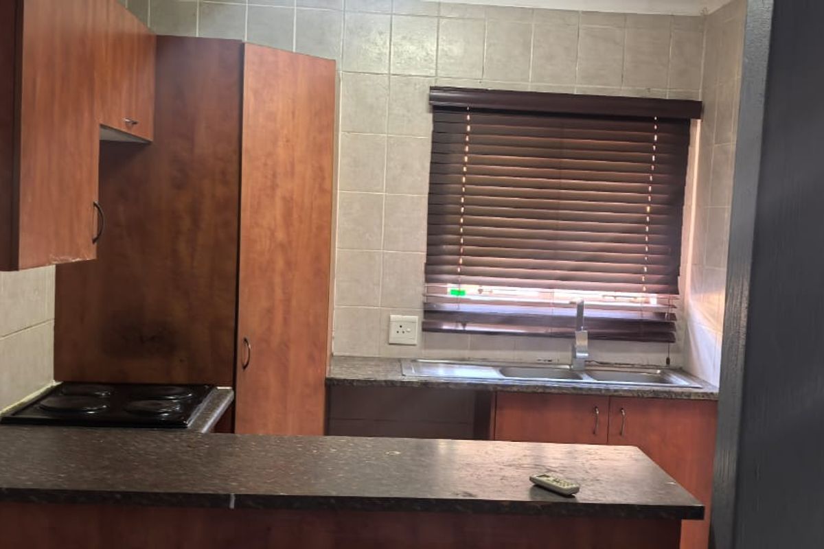 A functional kitchen featuring wood-look cabinetry, dark laminate countertops, an integrated electric hob, and a stainless steel sink with tiled backsplash.