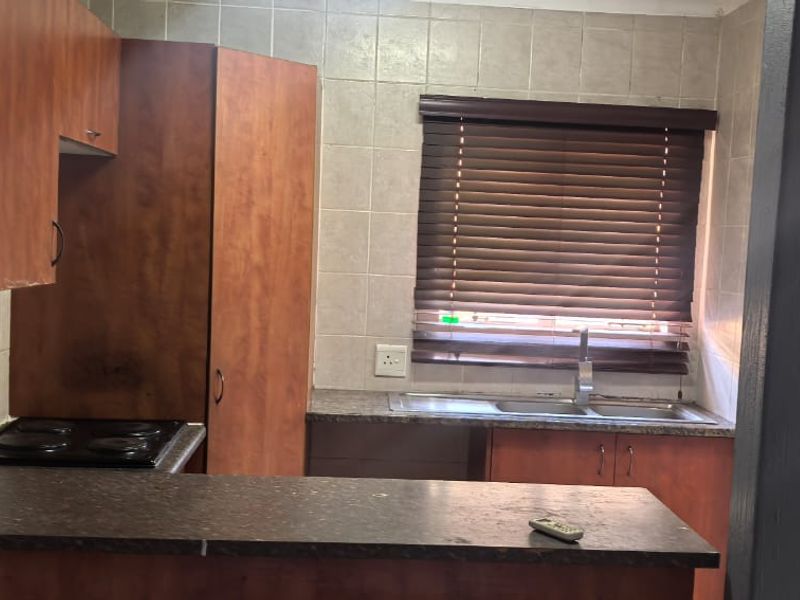 A functional kitchen featuring wood-look cabinetry, dark laminate countertops, an integrated electric hob, and a stainless steel sink with tiled backsplash.