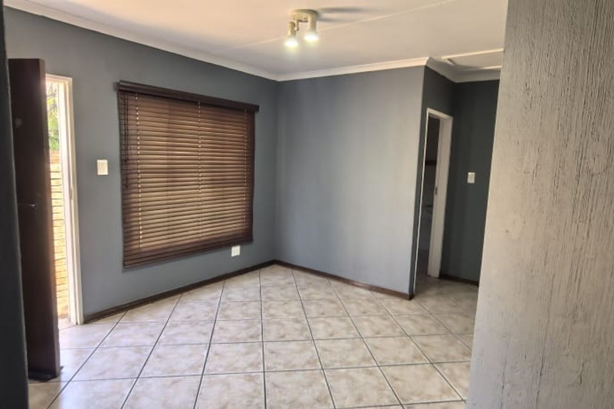 A bright, empty living room featuring neutral grey walls, tiled flooring, and venetian blinds, offering a clean and versatile space for personalization.