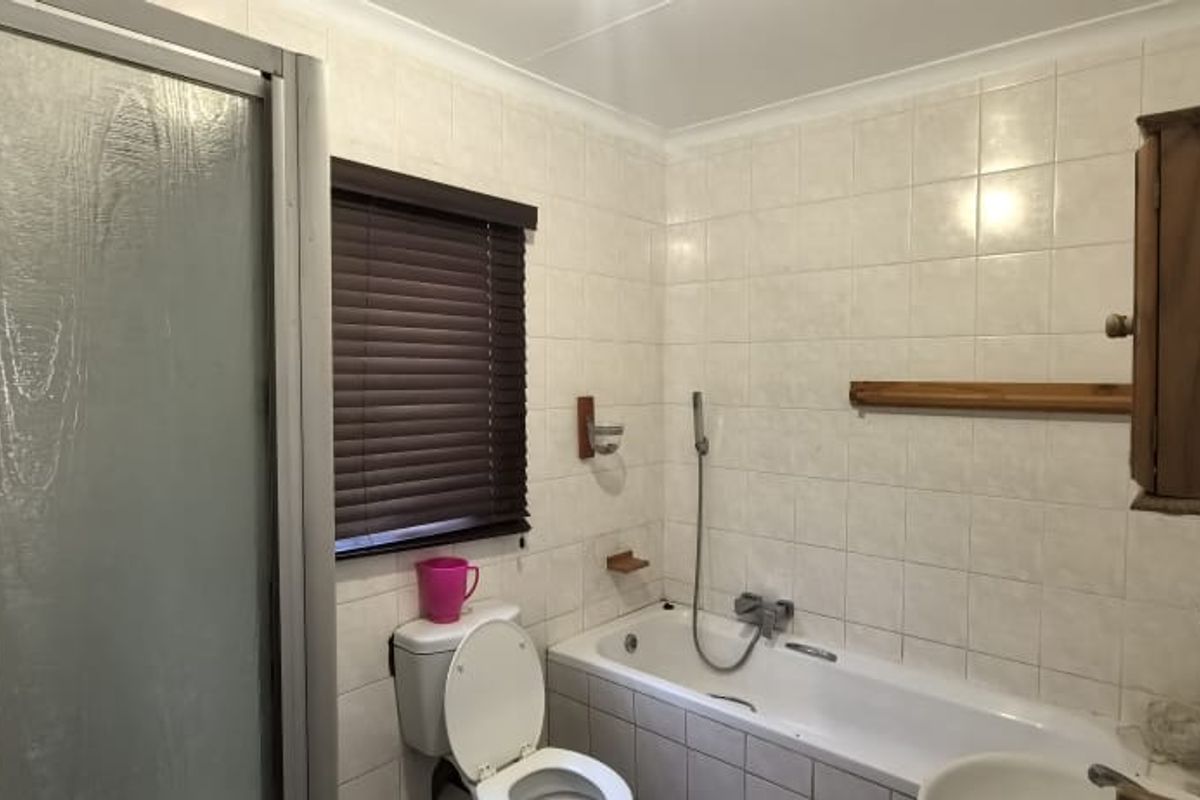 A functional bathroom featuring a combined bathtub and shower unit, tiled walls, and a window with fitted blinds.
