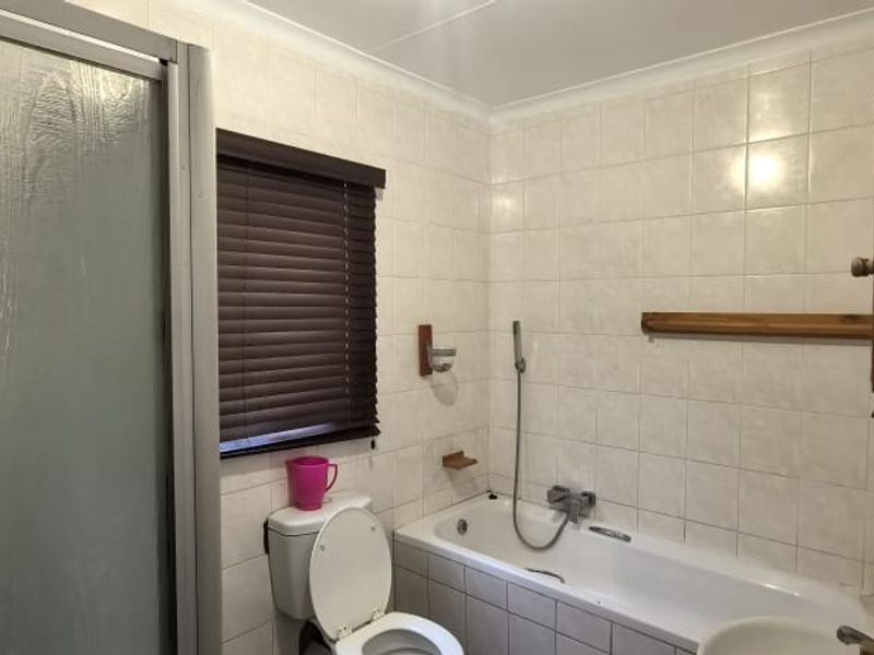 A functional bathroom featuring a combined bathtub and shower unit, tiled walls, and a window with fitted blinds.