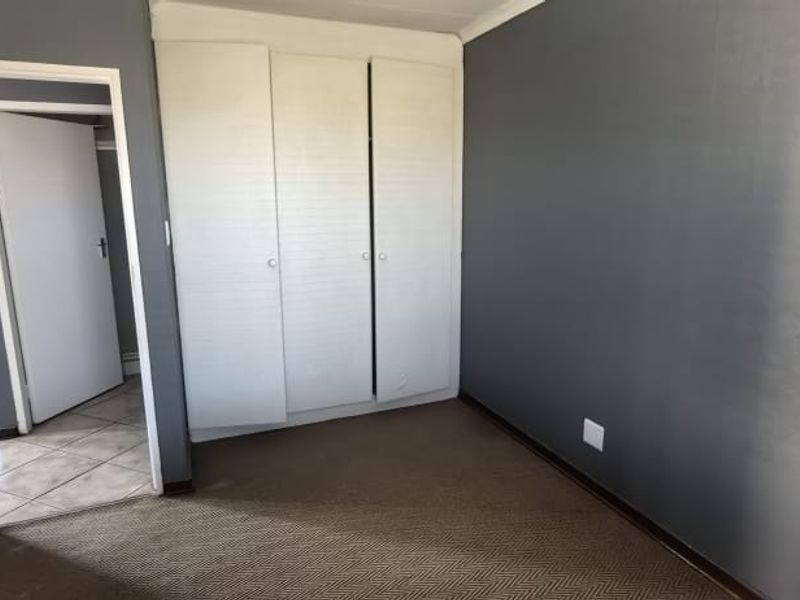 An empty bedroom featuring built-in cupboards, dark grey walls, and carpeted flooring, with an adjacent hallway visible through the doorway.