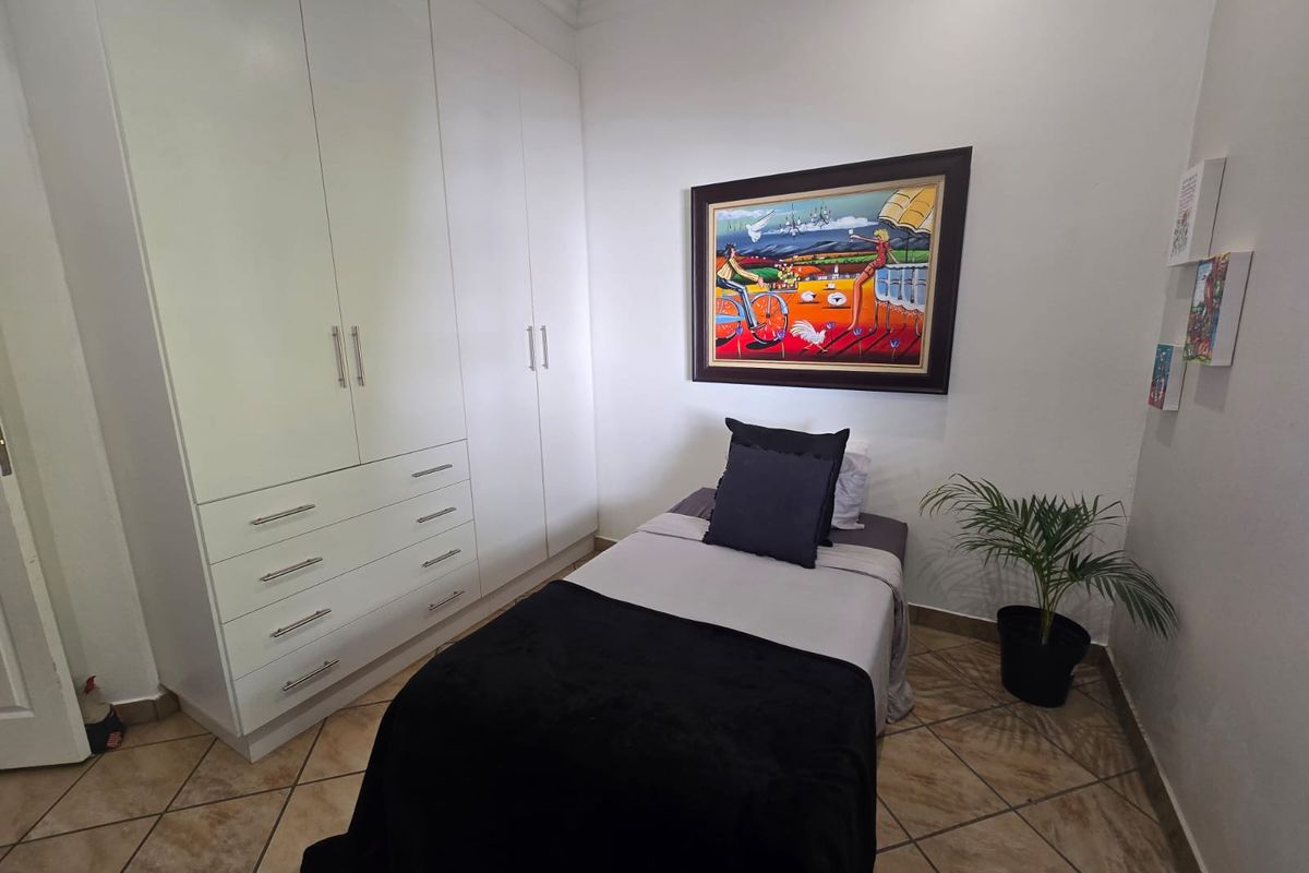 A compact bedroom featuring white built-in wardrobes with ample storage and durable tiled flooring.